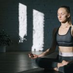 A woman meditates in a serene, sunlit room, embodying focus and tranquility.