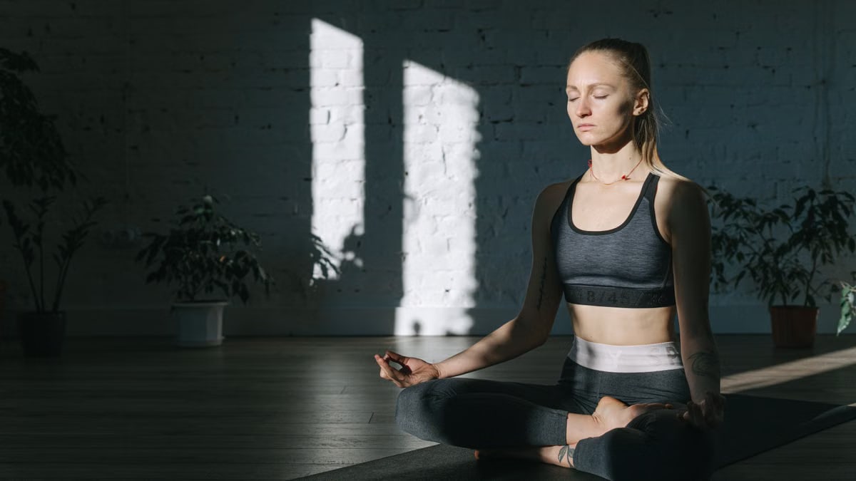 A woman meditates in a serene, sunlit room, embodying focus and tranquility.